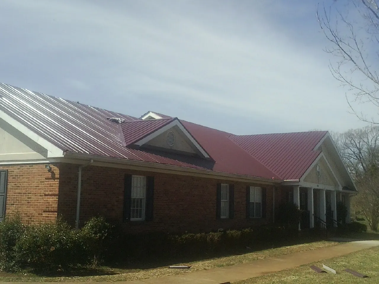 Red metal roof with gabled entries on a long brick building, from a Hail Damage Roof Repair job in Wacissa