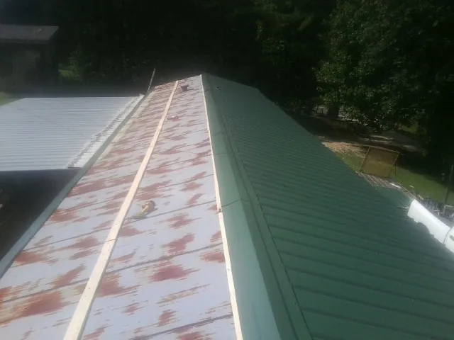 Old rusted panels beside newly installed green metal roofing — Wind Damage Roof Repair by Roofing Brothers in Wacissa