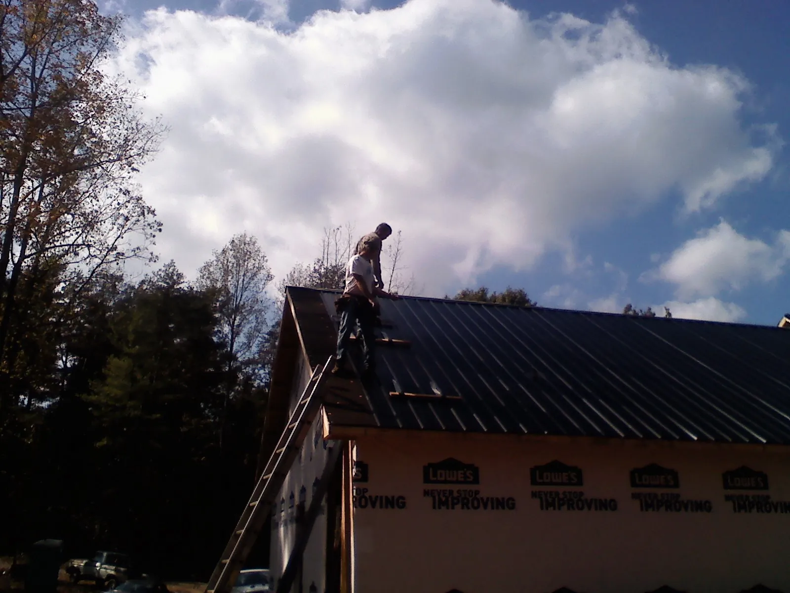 Roofer fastening dark metal panels high against a cloudy sky, from a Roof Inspection job in Wacissa